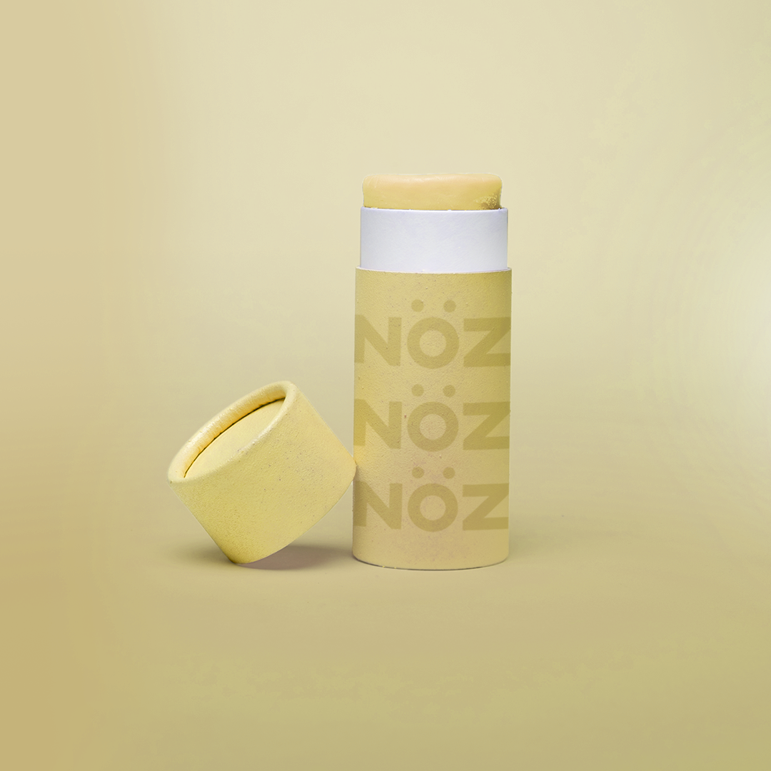 Opened yellow Nöz sunscreen stick with cap leaned up against left side of sunscreen stick.